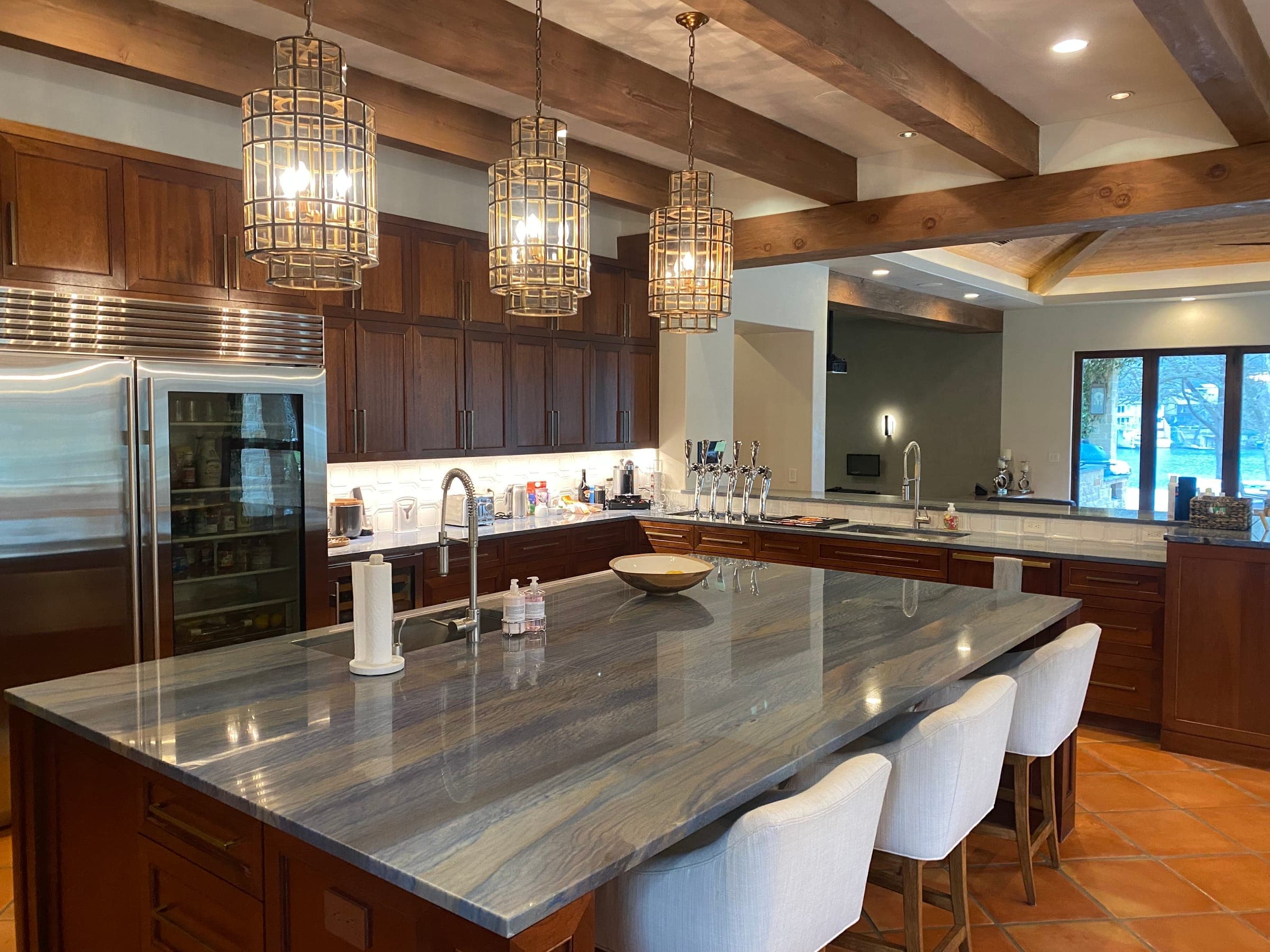 Kitchen with exposed beams, cage pendants and a long veined stone island